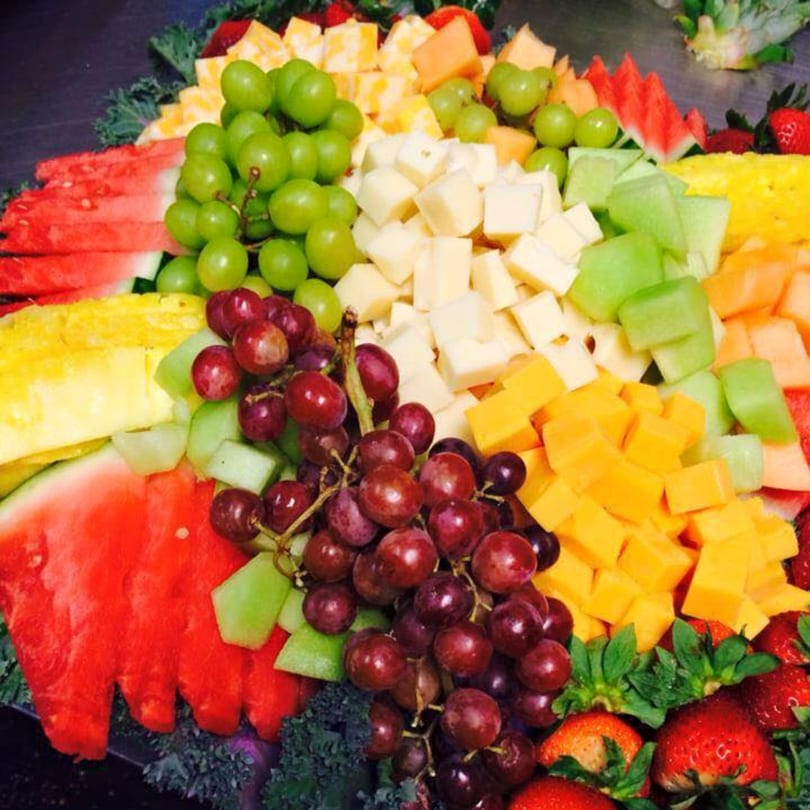 A colorful fruit and cheese platter featuring grapes, watermelon, pineapple, cantaloupe, and strawberries.