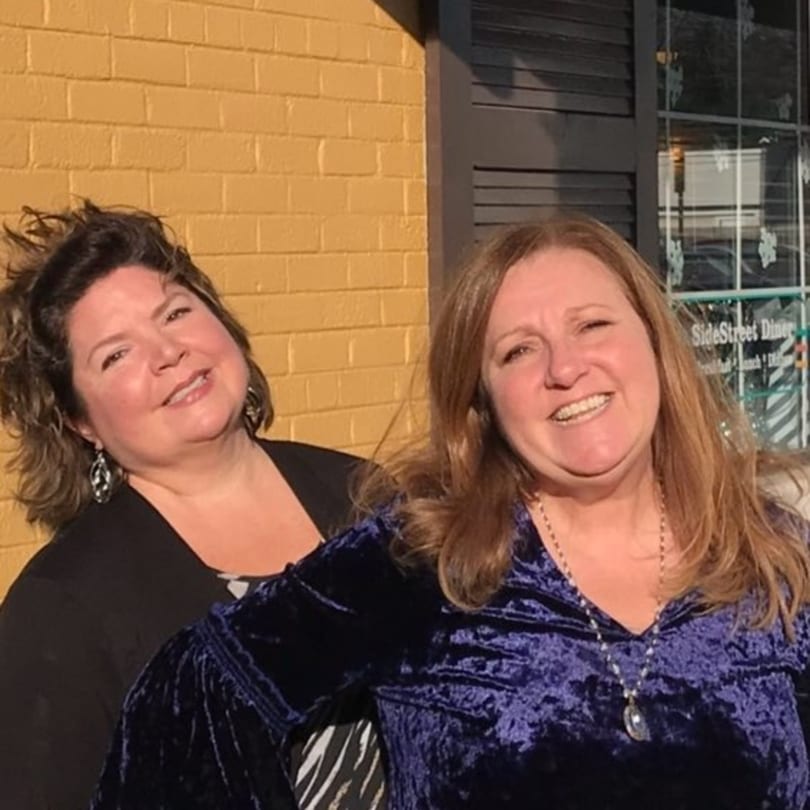 Two smiling women, one in black and one in purple, stand outside the Side Street Diner.
