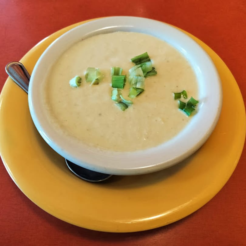 Creamy soup topped with chopped green onions in a white bowl on a yellow plate at Side Street Diner.