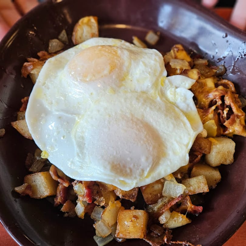 Side Street Diner's breakfast hash with fried eggs, potatoes, onions, and bacon in a brown bowl.