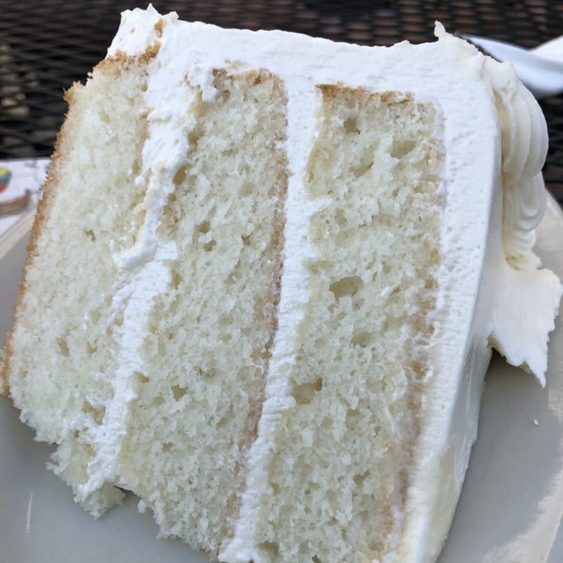 A thick slice of white layer cake with white frosting on a plate at Side Street Diner.