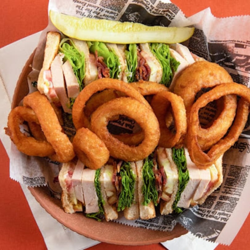 Side Street Diner's club sandwich with turkey, bacon, lettuce, and onion rings, served with a pickle.